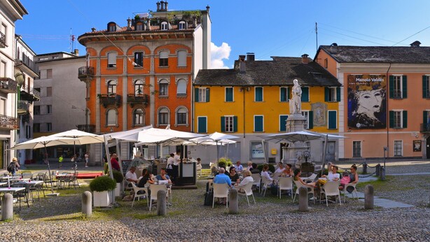 An outdoor café with tables and chairs, surrounded by colorful buildings.