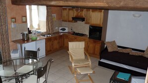 Una cocina compacta con armarios de madera, una mesa de comedor con sillas, un sofá y una pequeña mesa con una carpeta.