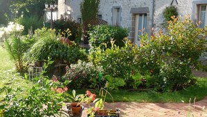 Un jardín con plantas en macetas y un sendero de ladrillo que lleva a un edificio de piedra con un letrero 'X'.