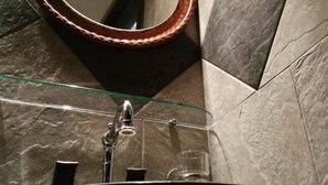 A bathroom with a glass sink, a copper basin, a mirror, and a modern design with geometric wall tiles. - Xenios Zeus (Aristotelis)