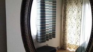 A room with a large mirror, a bed with striped bedding, a small table, and curtains with a floral pattern. - Xenios Zeus (Aristotelis)