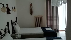 A hotel room with two single beds, a radiator, a wall-mounted air conditioner, and a window with sheer curtains. - Xenios Zeus (Aristotelis)