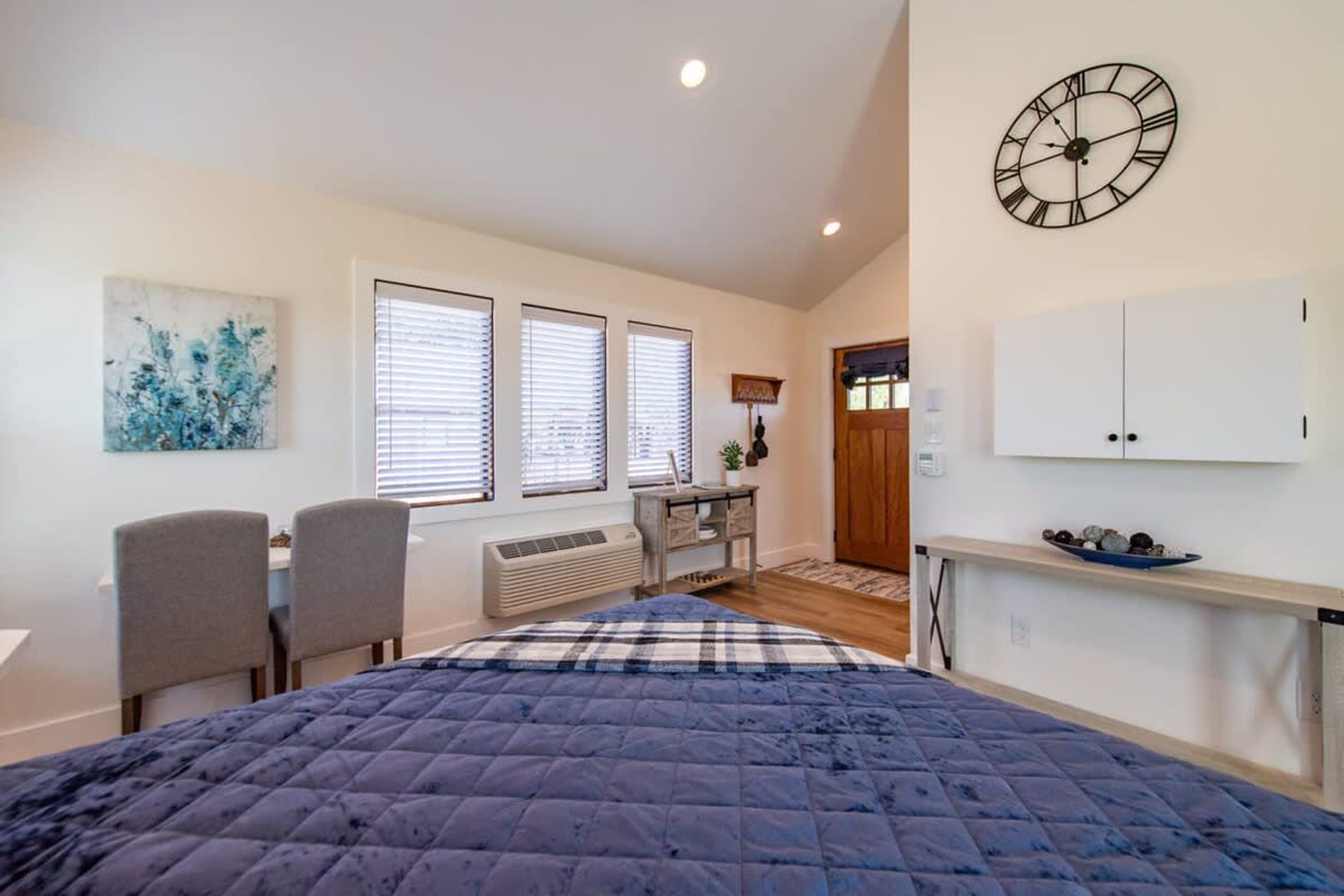 A bedroom with a bed, a desk, a chair, a clock, and a wardrobe.