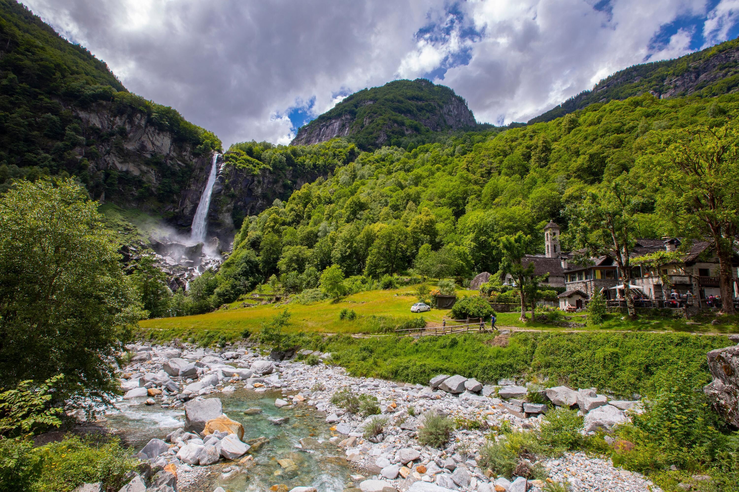 A mountainous landscape with a waterfall, a river, and a building with a tower.