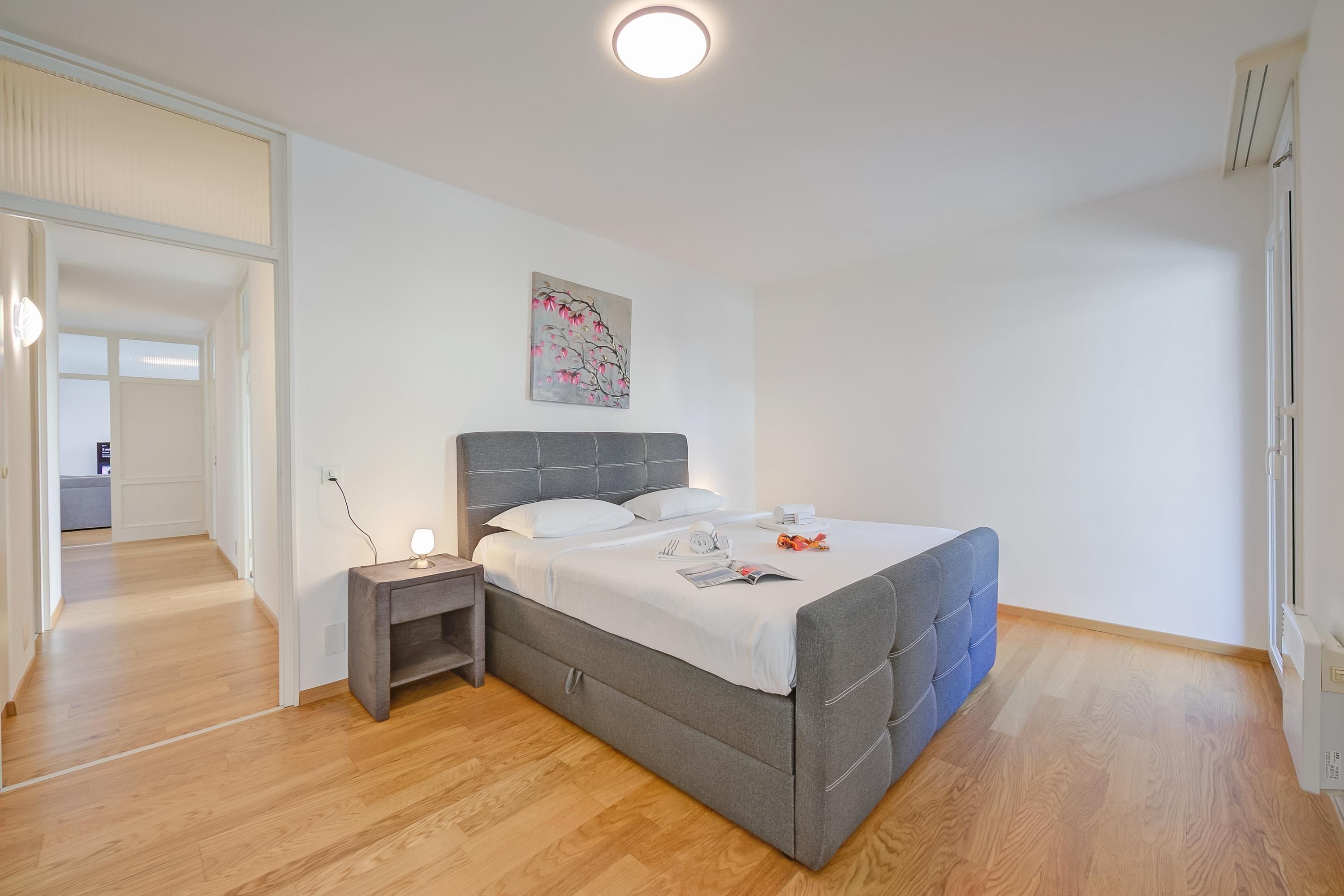 A bedroom with a bed, bedside table, and a painting on the wall.