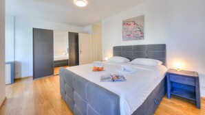 Une chambre moderne avec un grand lit, une table de chevet avec une lampe, un tableau au mur et une porte donnant sur une autre pièce.
