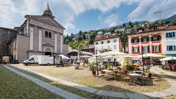 Une place avec des tables en plein air, un camion de livraison blanc et un bâtiment historique surmonté d’un dôme.