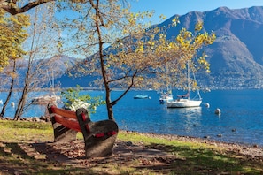 A bench by a lake with boats and mountains in the background. - Casa Al Molo in Locarno (Locarno)