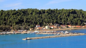 A marina with boats docked, surrounded by a forested hillside and buildings with red roofs. - Maritinas Stone Apartment On The Beach (Pyrgos)