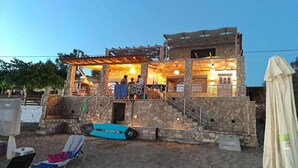 A stone building with a covered outdoor area, a pool, and a beach chair area. - Maritinas Stone Apartment On The Beach (Pyrgos)