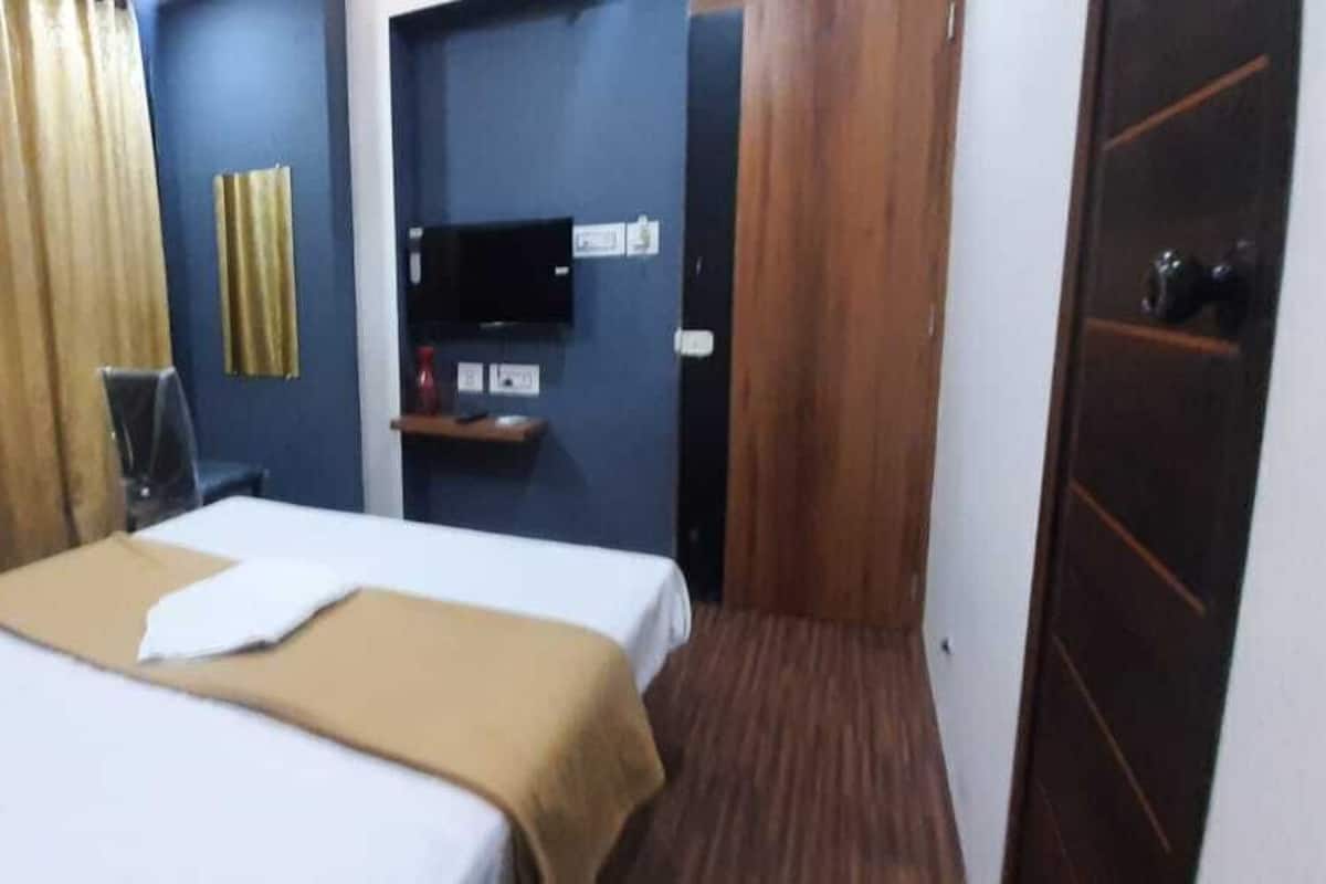 A hotel room with a bed, a television, a shelf, and a door.