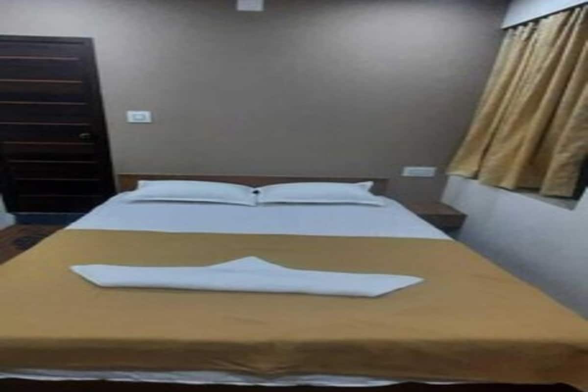 A single bed with a brown bedspread in a room with wooden flooring, a ceiling fan, and a window with curtains.
