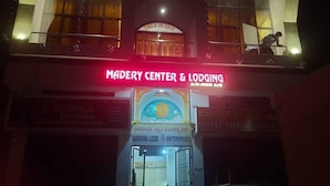 La entrada de un edificio con un letrero que dice 'MADERY CENTER & LODGING' y 'TASHODHA LAKHM ENTERPRISES'.