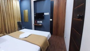Una habitación de hotel con cama, televisión, repisa con objetos y una puerta.