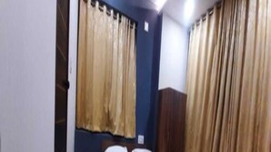Una habitación pequeña con cama individual, cabecera de madera, mesita de noche y dos cortinas.