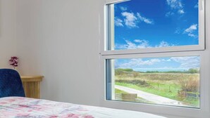 Una habitación con cama, una silla, una mesa de madera y una ventana con vistas al paisaje rural.