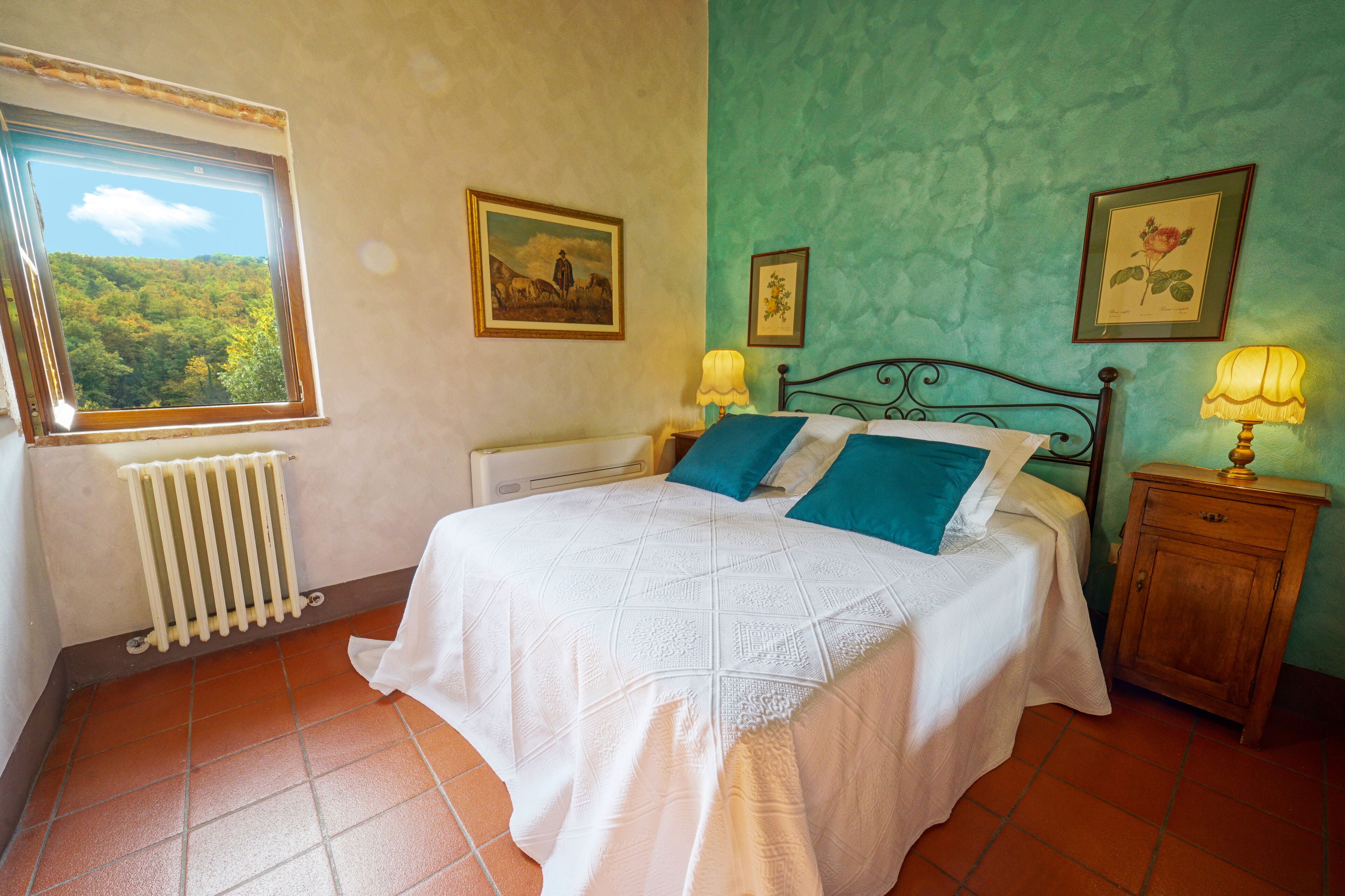 Ein Schlafzimmer mit einem Bett, einem Fenster mit Blick auf einen Wald, einem Heizkörper und zwei Wandlampen.