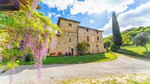 A stone building with a gravel driveway and a garden with purple flowers.