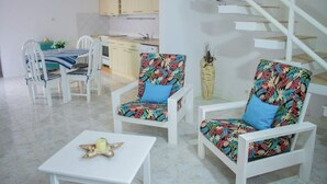 Un salon moderne avec des meubles blancs, un escalier et une cuisine en arrière-plan.