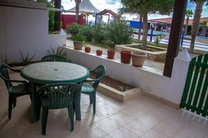 Un patio con una mesa redonda y cuatro sillas, rodeado de plantas en macetas y un pequeño jardín.