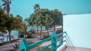 Un escalier avec des rampes de couleur turquoise mène à un balcon qui donne sur un espace paysager agrémenté d’arbres et offrant une vue sur la mer.