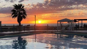 Une piscine avec vue sur le coucher de soleil, un palmier et un poste de surveillance pour les sauveteurs.