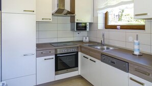 A modern kitchen with white cabinetry, a built-in oven, a microwave, and a window with a view of greenery. - House Kolpa Paradise Whirlpool And Sauna (Metlika)