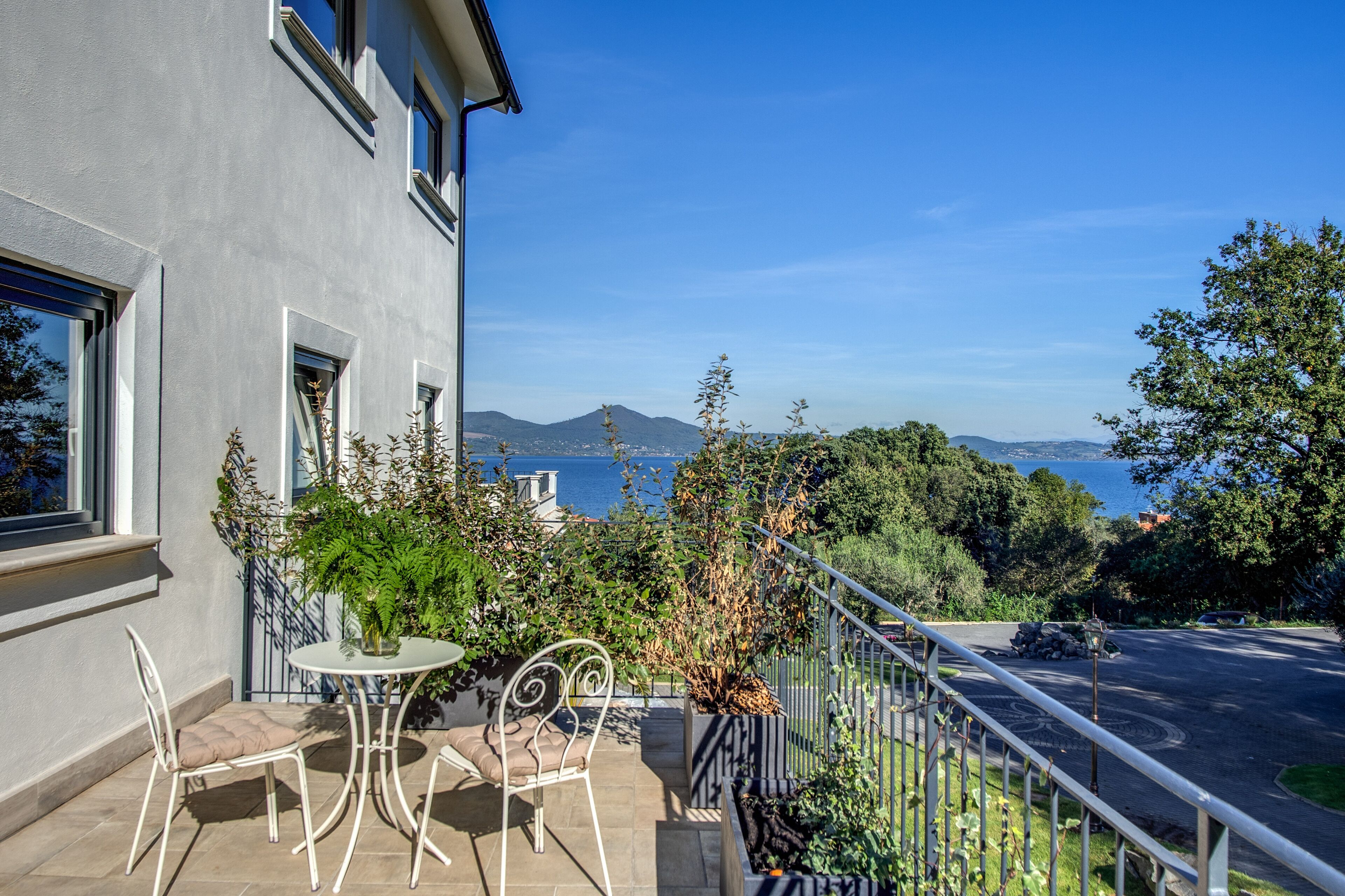 A balcony with a table and chairs, overlooking a body of water and hills.