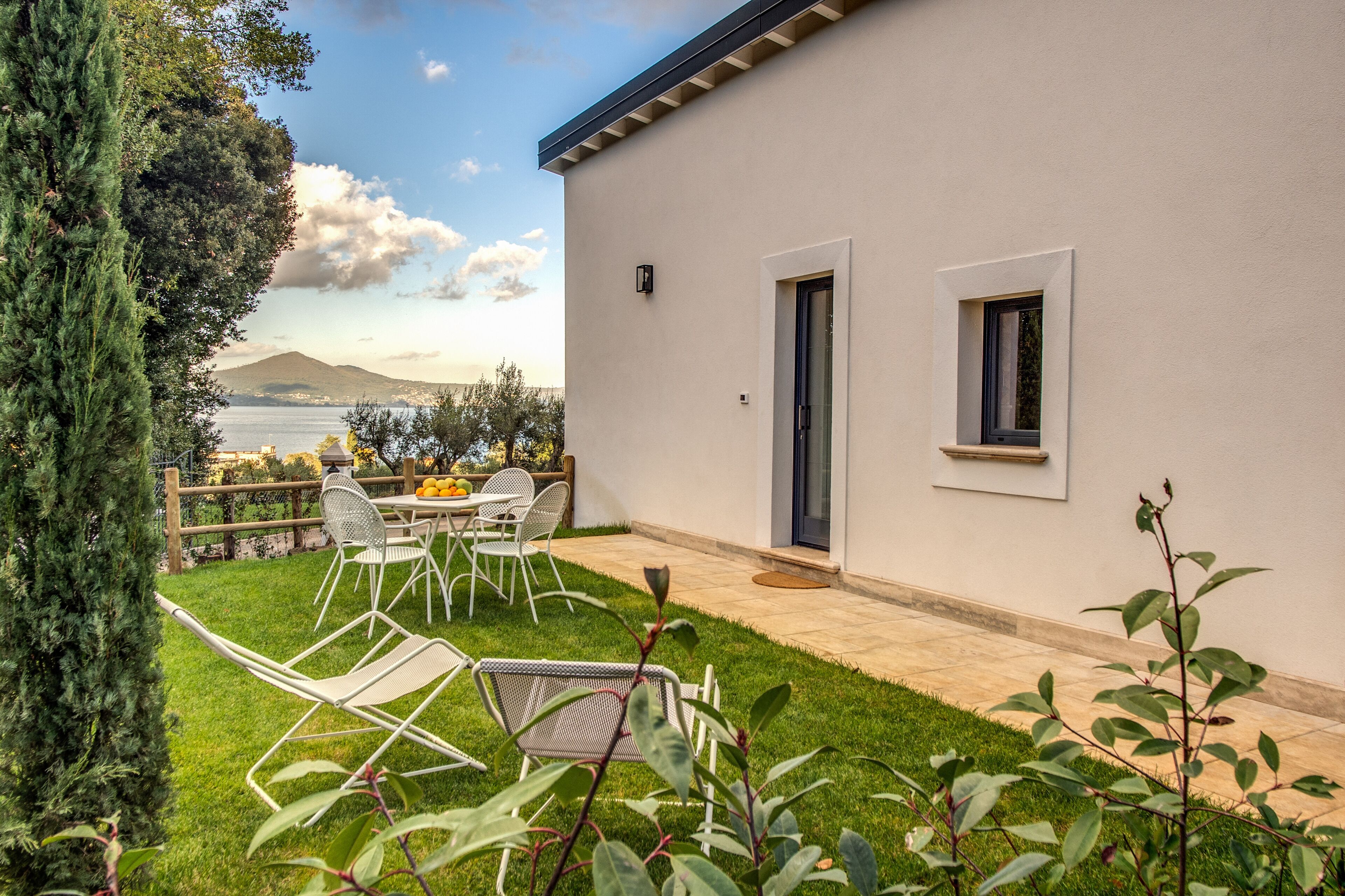 A modern house with a patio, outdoor seating, and a view of a body of water and mountains.