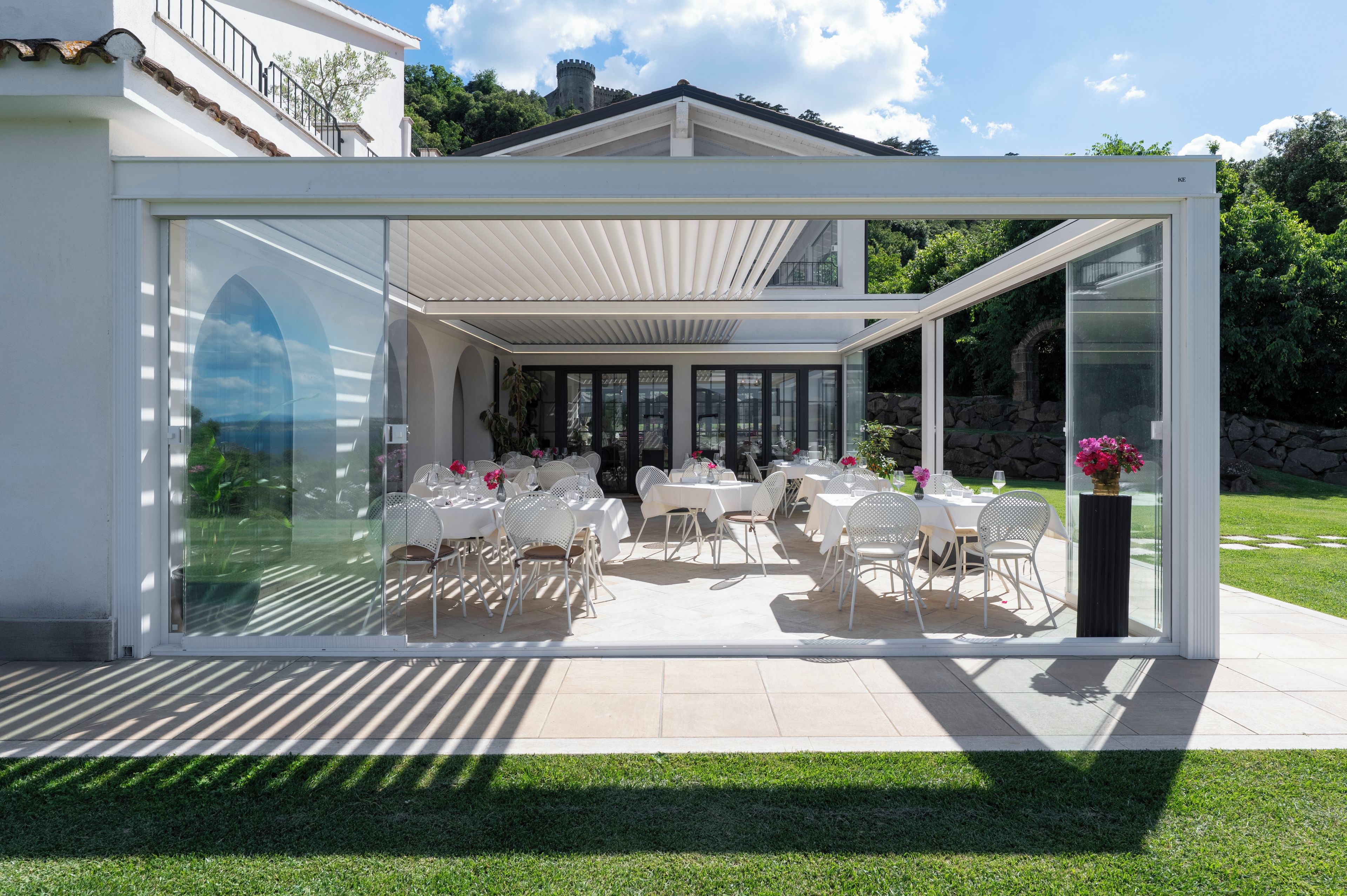 A modern glass-enclosed patio with outdoor seating and a view of a castle in the background.