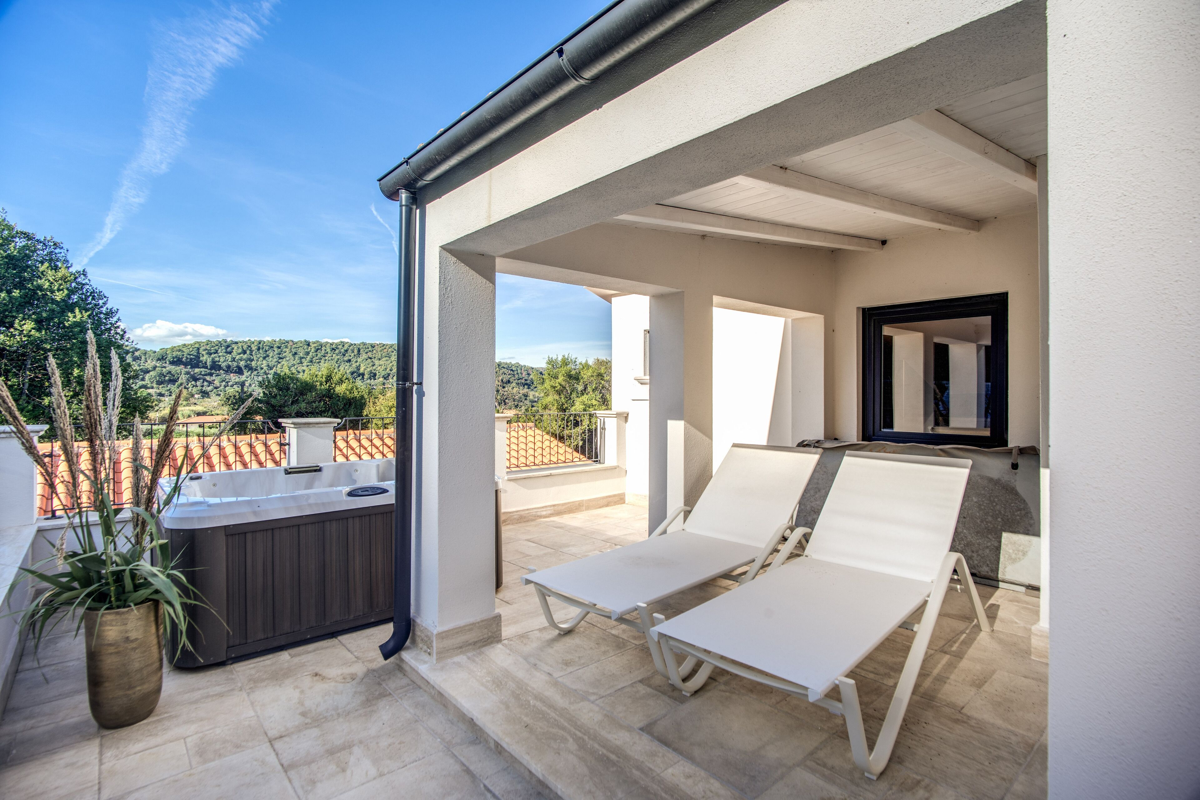 Uma área externa coberta com duas poltronas brancas, uma banheira de hidromassagem e vista para uma encosta.
