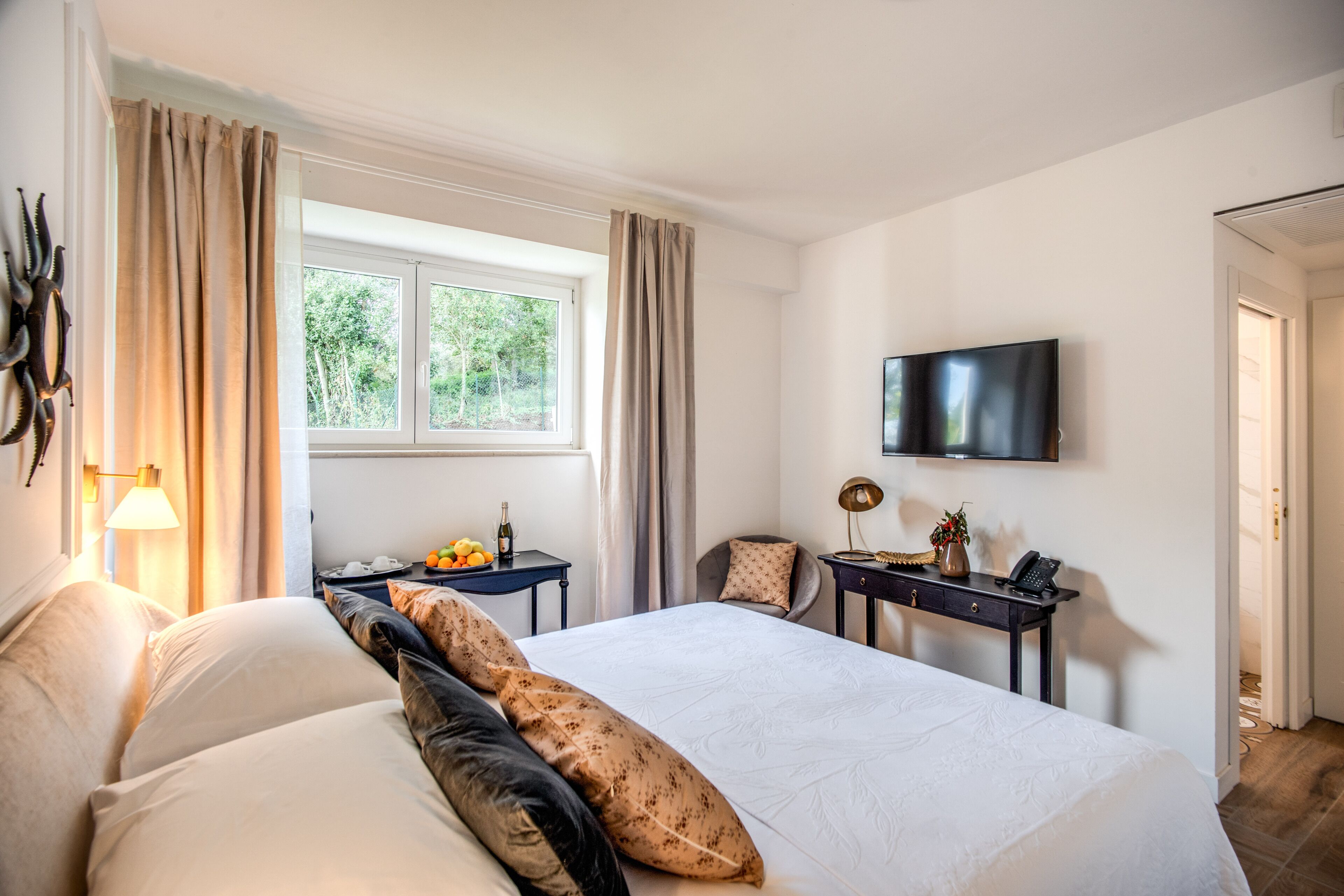 A hotel room with a large bed, a desk with a lamp, a TV, and a window with curtains.