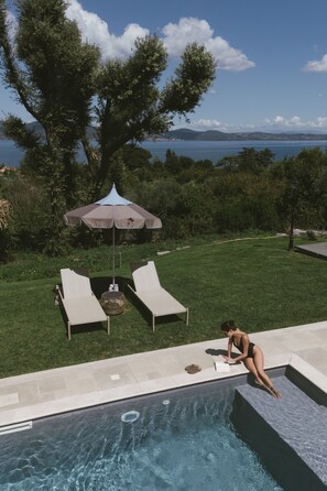 A swimming pool with a view of the sea, two lounge chairs, and an umbrella. - Vigna Caio Relais & Spa (Bracciano)