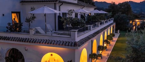 Una villa moderna con un espacio exterior cubierto, varios arcos y un jardín cuidado.