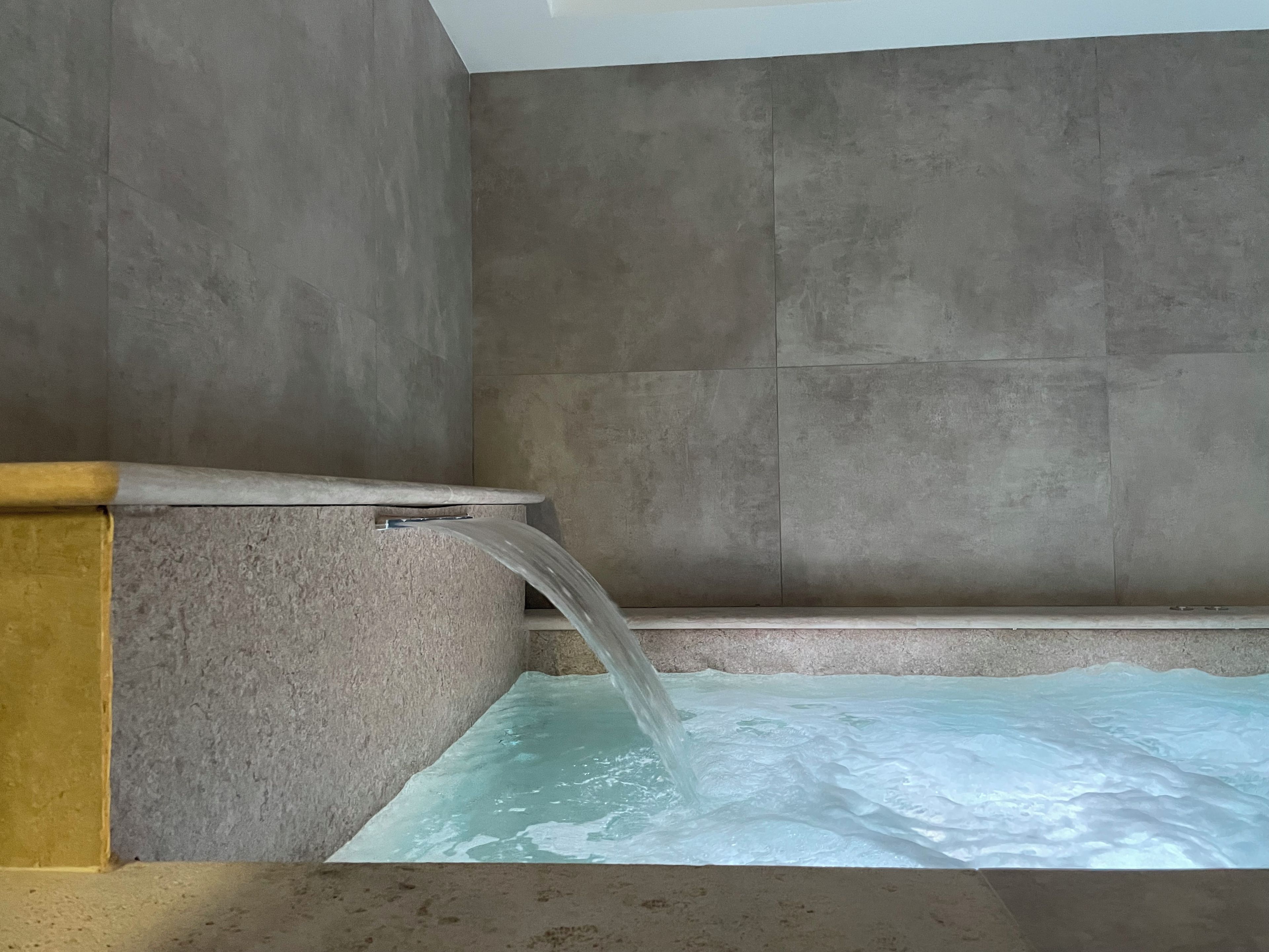 Una bañera con una cascada de agua, un borde de madera y una pared con azulejos.