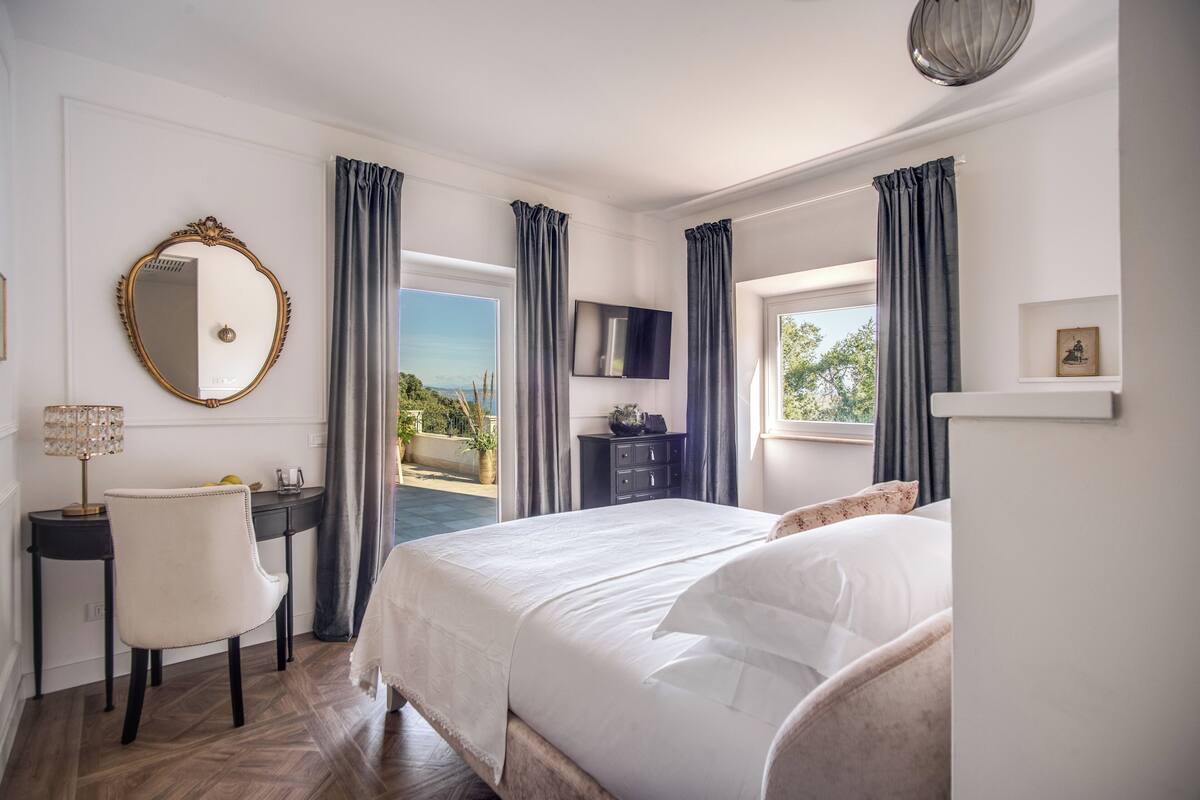 Ein Schlafzimmer mit Bett, Schreibtisch, Stuhl, Fernseher und einem Fenster mit Vorhängen.