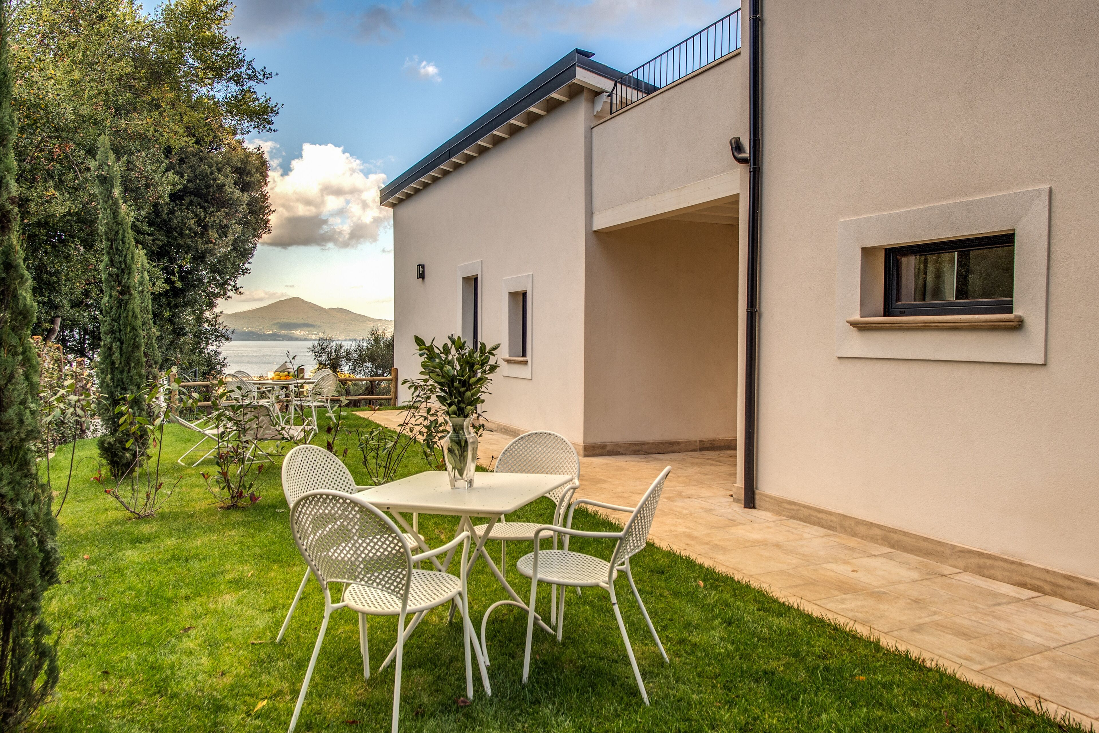 Une maison moderne dotée d’un patio, d’une table à manger avec des chaises, et offrant une vue sur une montagne et un lac.