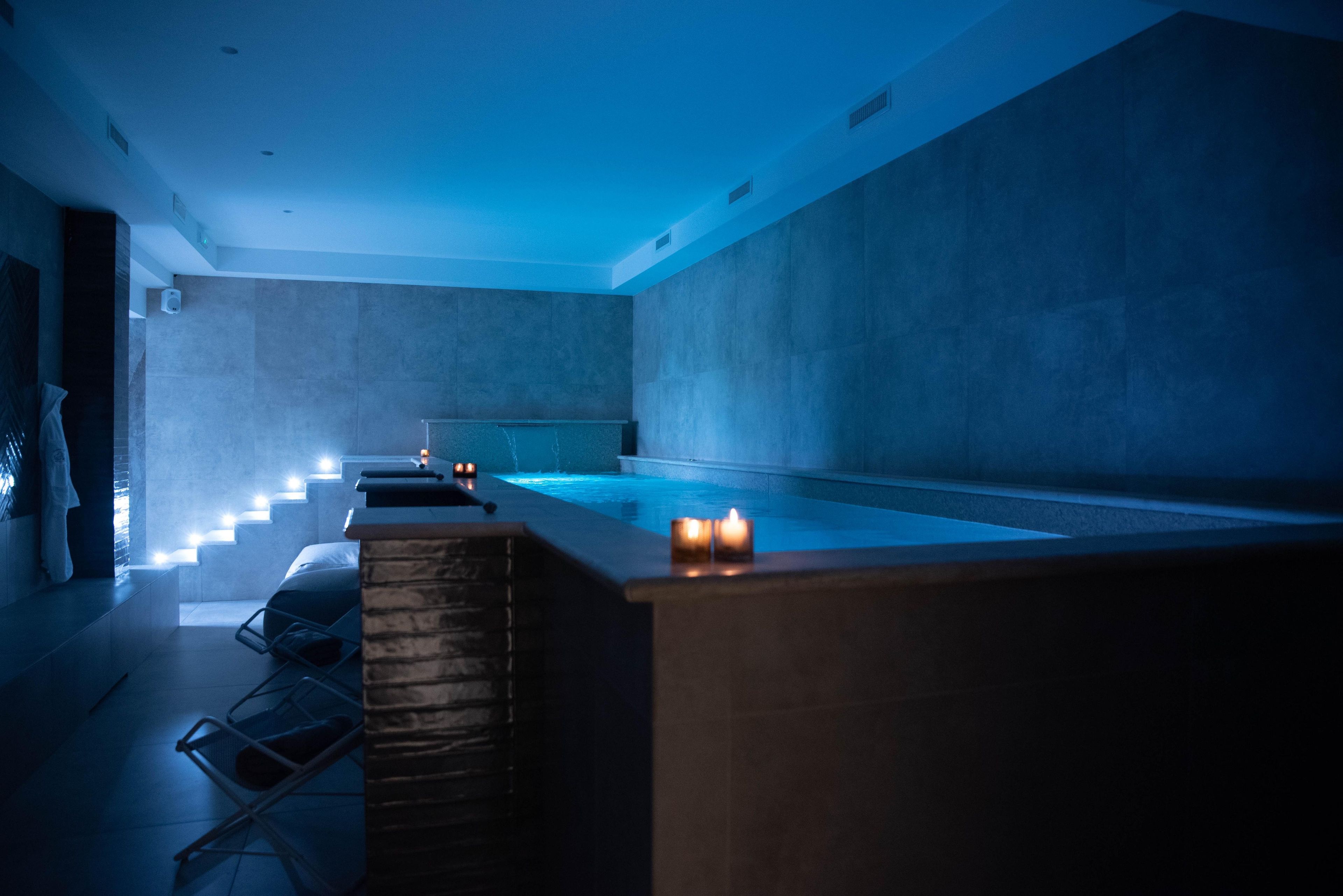 A modern spa with a large pool, a seating area with chairs, and candles for ambiance.