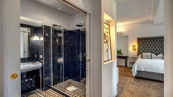 Un baño moderno con cabina de ducha de vidrio, piso de mármol y lavamanos blanco.