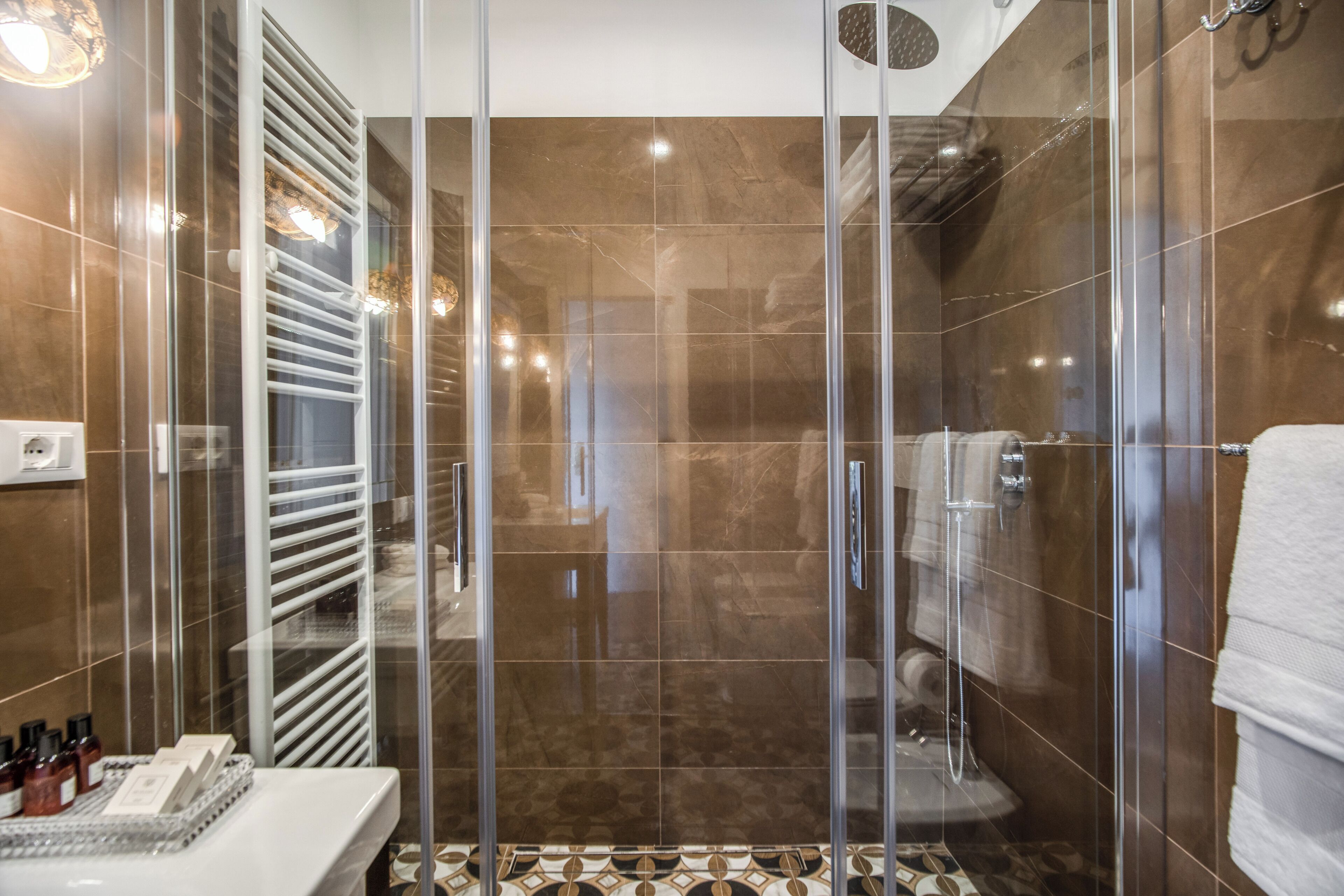Un baño moderno con cabina de ducha de vidrio, un lavamanos blanco y suelo estampado.