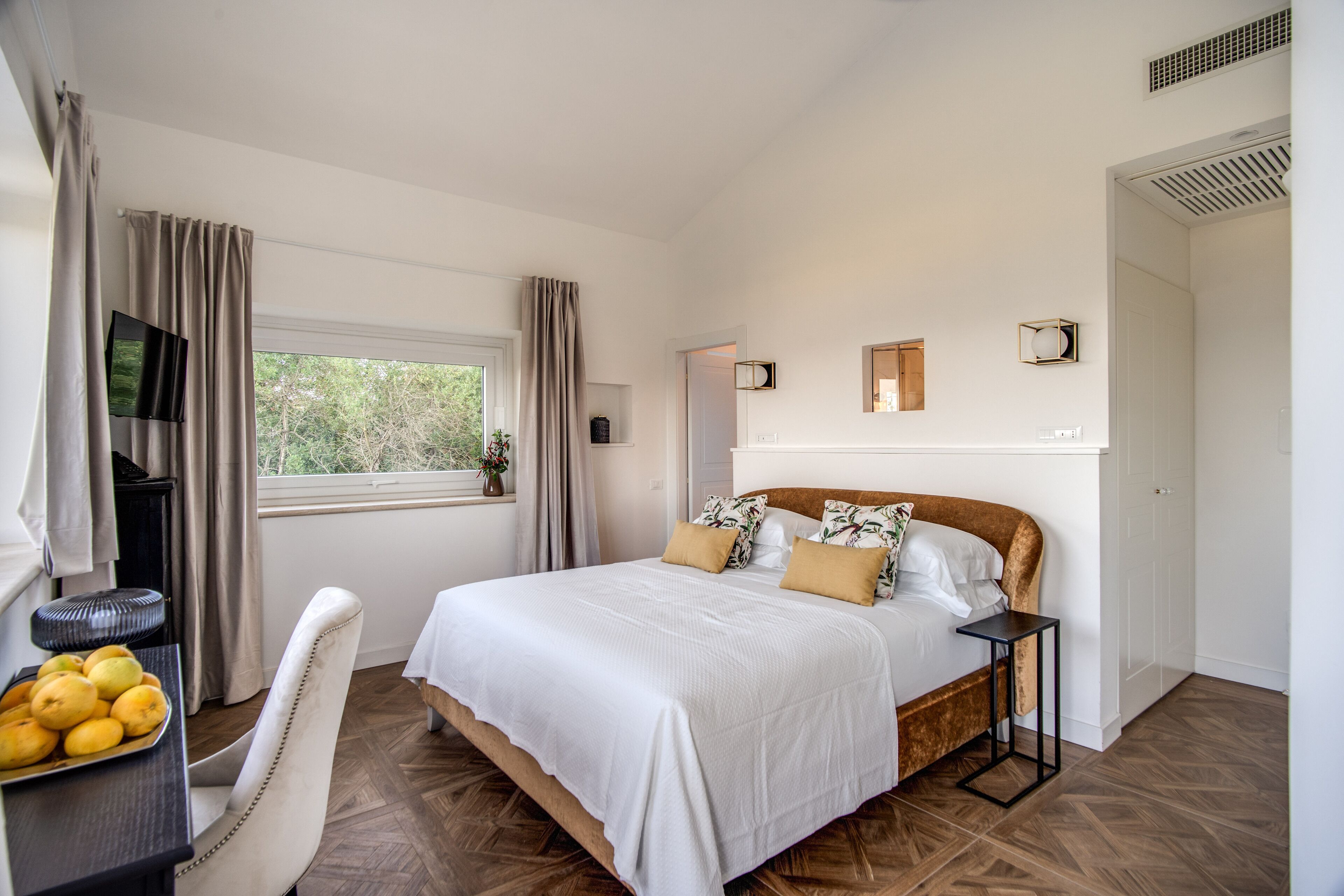A bedroom with a large bed, a desk with a chair, a television, and a window with curtains.