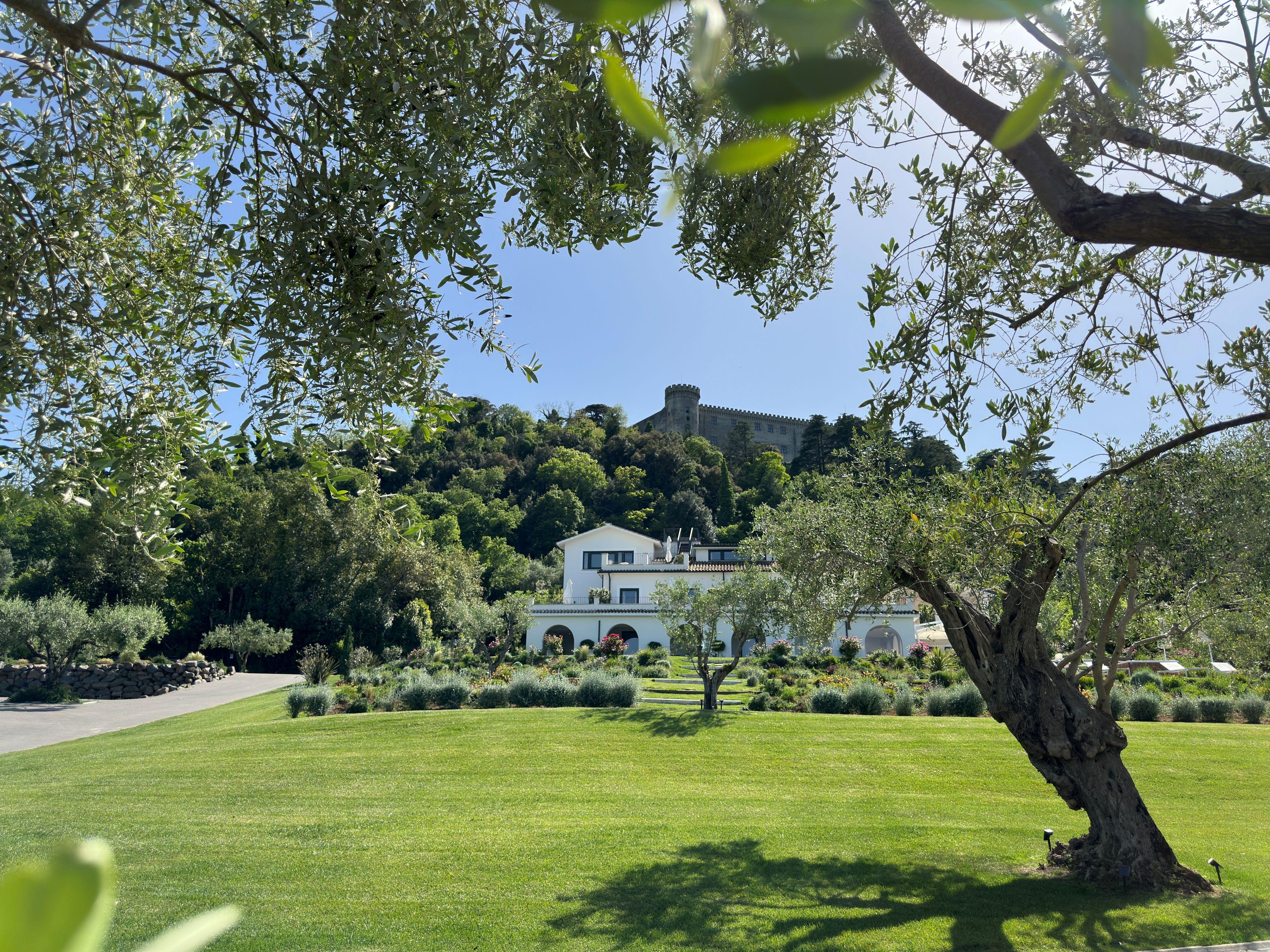 Een verzorgd gazon, een wit gebouw met balkon, en een kasteel op een heuvel in de verte.