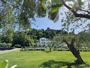 A well-maintained lawn, a white building with a balcony, and a castle on a hill in the background. - Vigna Caio Relais & Spa (Bracciano)