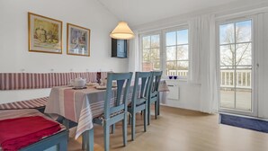Comedor con una mesa preparada para cuatro, un banco con cojines y vistas al exterior a través de amplias ventanas.