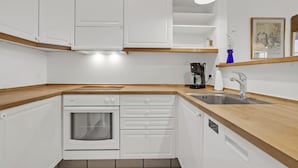Una cocina compacta con armarios blancos, horno empotrado, cafetera y lavaplatos.
