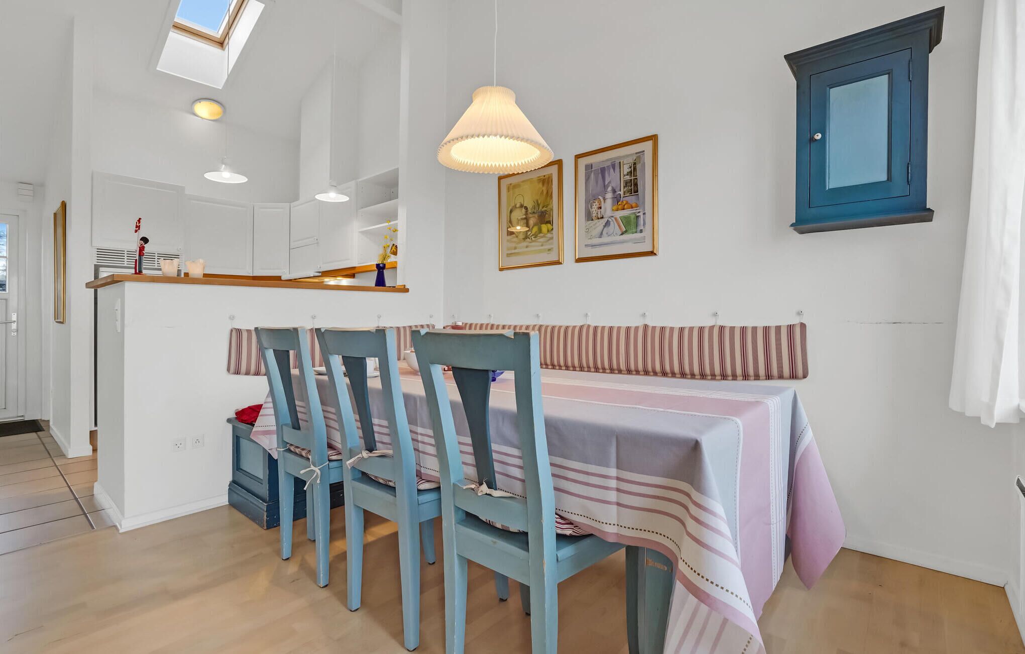 A dining area with a table set for four, a blue chair, and a hanging light fixture.