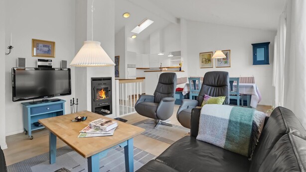 Una sala moderna con televisor de pantalla plana, chimenea, dos sillones de cuero, un sofá y un comedor con mesa y sillas.