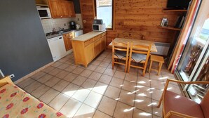 A compact kitchen with wooden cabinets, a microwave, and a small dining area with a table and chairs. - 002 Rochebrune - Chalet l'Hysope (La Salle-les-Alpes)