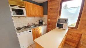 A compact kitchen with wooden cabinets, a built-in microwave, a coffee maker, and a window with a view. - 002 Rochebrune - Chalet l'Hysope (La Salle-les-Alpes)