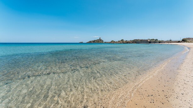 A clear beach with calm waters, a sandy shore, and a rocky outcrop in the distance. - One bedroom apartment (4 people) Premium - Residence Baia delle Palme (Sardegna)